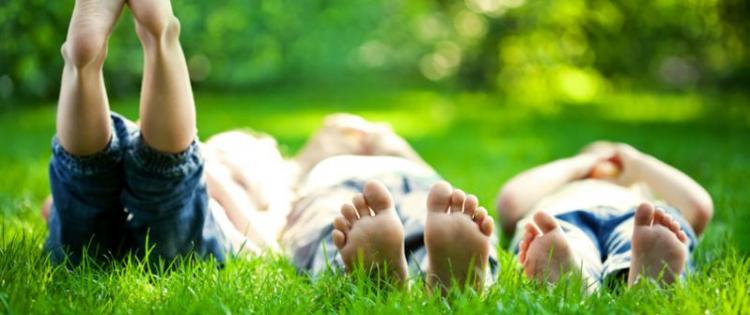 Three kids lying barefoot in the grass. Their feet are close to the camera. One kid has his feet raised to the sky.
