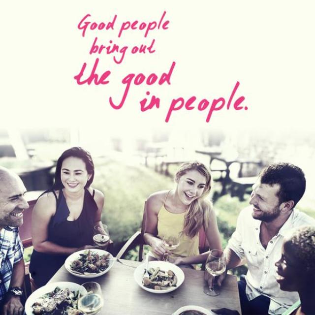 Image of several people eating at a table and laughing together.  The caption reads, "Good people bring out the good in people."