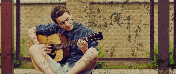 Young man sitting with legs crossed and playing guitar outside